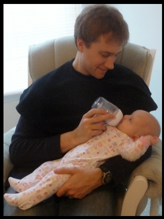 Daddy wearing Peek-a-Bye-Baby Cover while infant drinks bottle